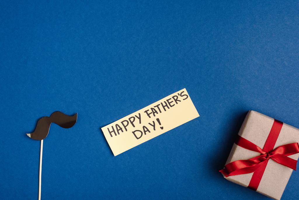 górny widok papieru dekoracyjne sztuczne wąsy z tektury, pudełko z upominkami i kartka z napisami szczęśliwy dzień ojców - Zdjęcie, obraz