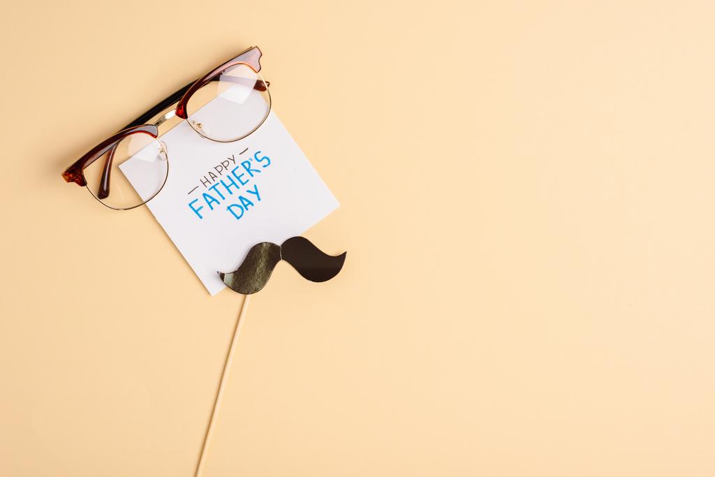 top view of mens glasses, decorative paper mustache and greeting card with lettering happy fathers day on beige background - Photo, Image