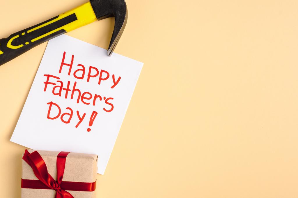 Draufsicht auf Hammer, Geschenkbox und Grußkarte mit Schriftzug Happy Vatertag auf beigem Hintergrund - Foto, Bild