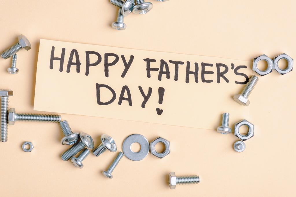 bovenaanzicht van metalen moeren en bouten en beige wenskaart met handgeschreven belettering gelukkige vaderdag op beige achtergrond  - Foto, afbeelding