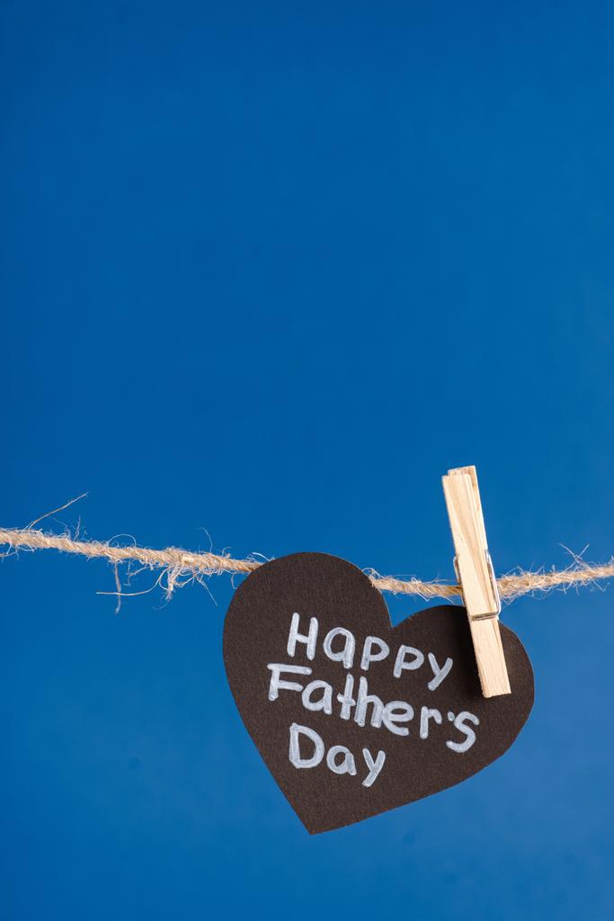 Μαύρη χάρτινη καρδιά με λευκά γράμματα χαρούμενη ημέρα πατεράδων κρεμασμένη σε σχοινί με μανταλάκια απομονωμένη στο μπλε - Φωτογραφία, εικόνα