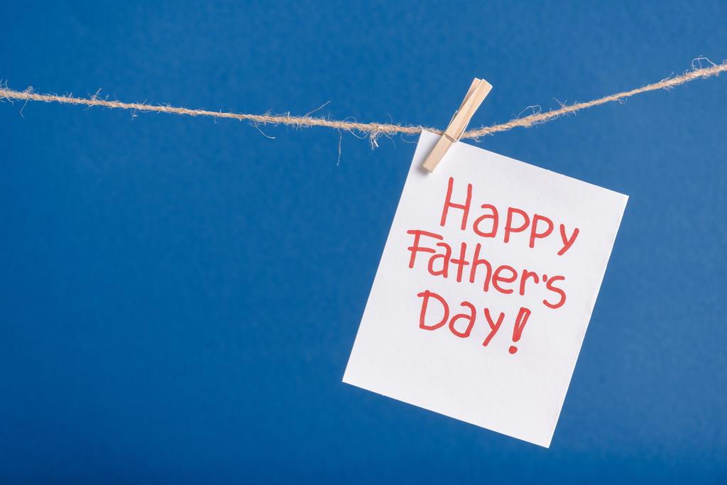 Witte papier wenskaart met rode letters gelukkige vaders dag opknoping op touw met wasknijpers geïsoleerd op blauw - Foto, afbeelding
