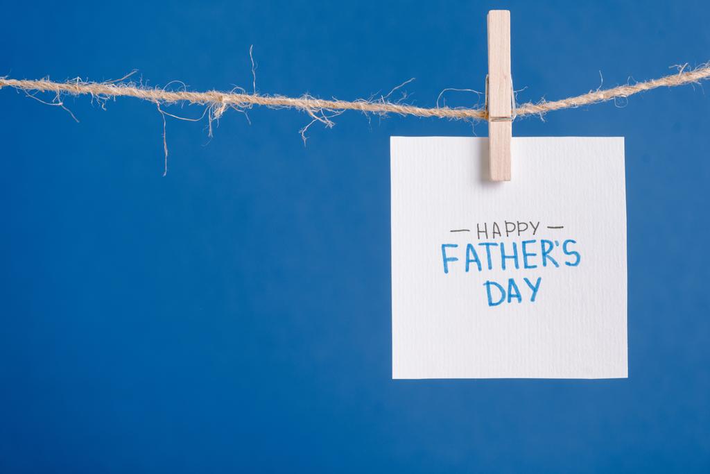 Carte de vœux blanche avec lettrage joyeuse fête des pères accrochée à une corde avec des pinces à linge isolées sur bleu
 - Photo, image