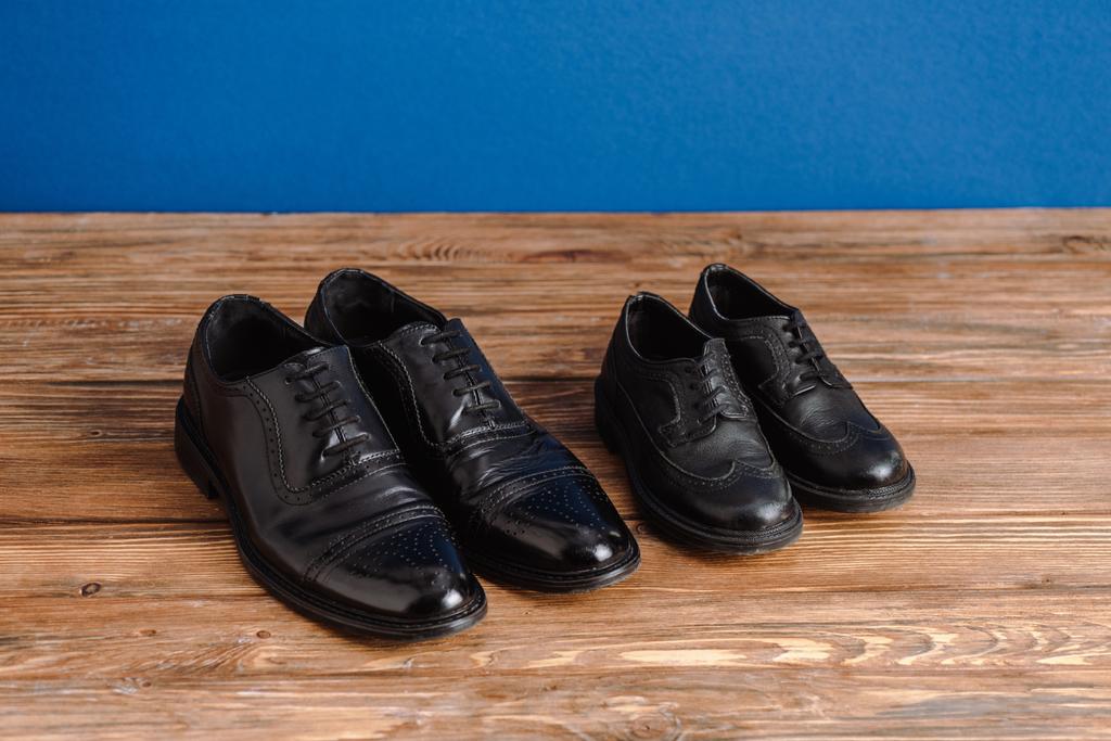 Vysoký úhel pohledu na černé pánské a dětské boty izolované na modré - Fotografie, Obrázek