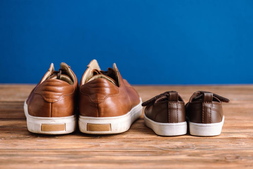 mens and childrens brown casual shoes on textured wooden surface isolated on blue, fathers day concept - Photo, Image
