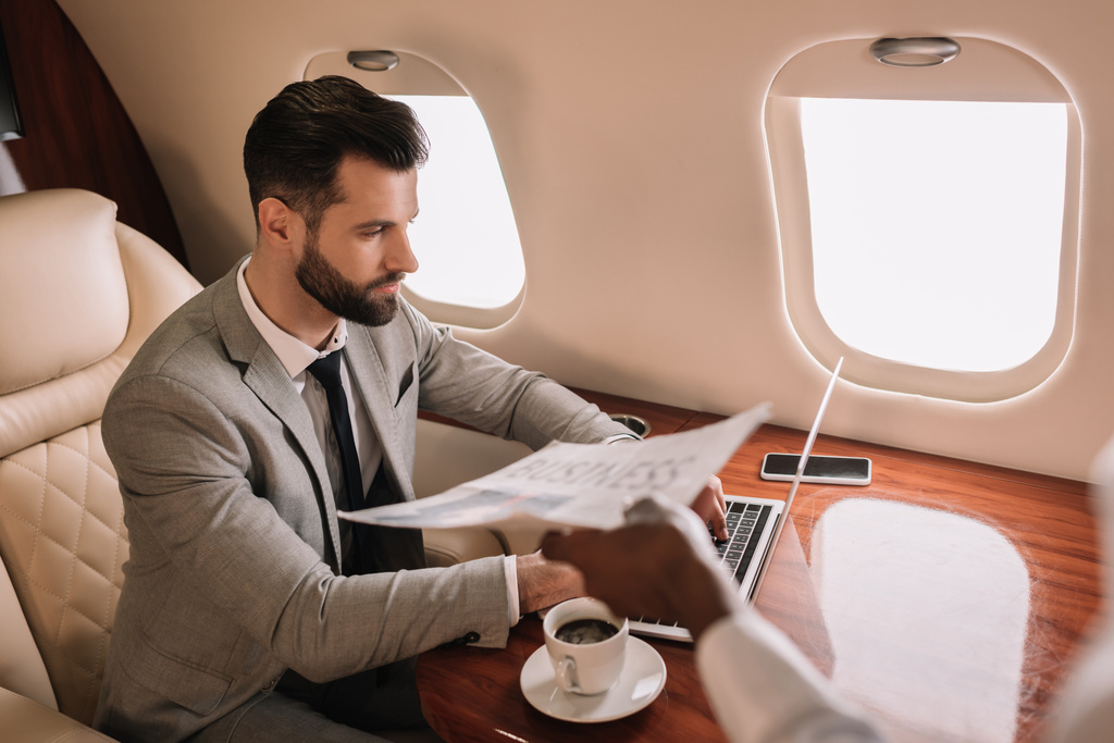 kivágott kilátás afro-amerikai stewardess ad újságot az üzletember dolgozik laptop privát jet - Fotó, kép