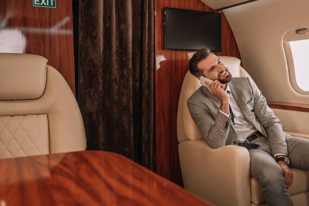 sonriente hombre de negocios hablando en el teléfono inteligente mientras viaja en jet privado
 - Foto, imagen