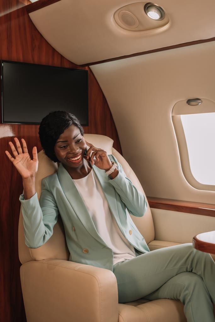 アフリカ系アメリカ人のビジネスマンが飛行機の中でスマホで話しながら手を振って - 写真・画像