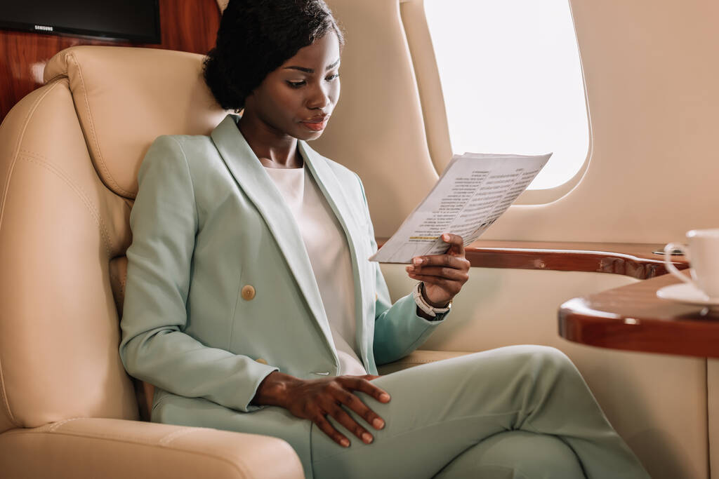 концентрована афроамериканська бізнес-леді читає документ в приватному літаку
 - Фото, зображення