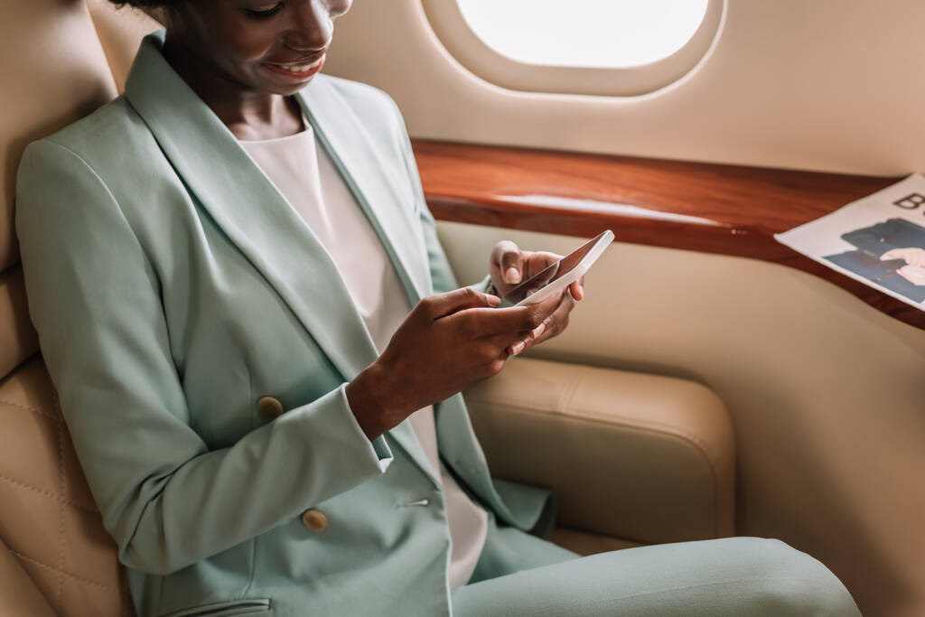 アフリカ系アメリカ人のビジネスマンが民間航空機でスマートフォンでチャットし - 写真・画像