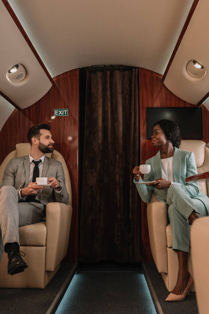 schöner Geschäftsmann und attraktive afrikanisch-amerikanische Geschäftsfrau schauen einander an, während sie Tassen Kaffee halten - Foto, Bild