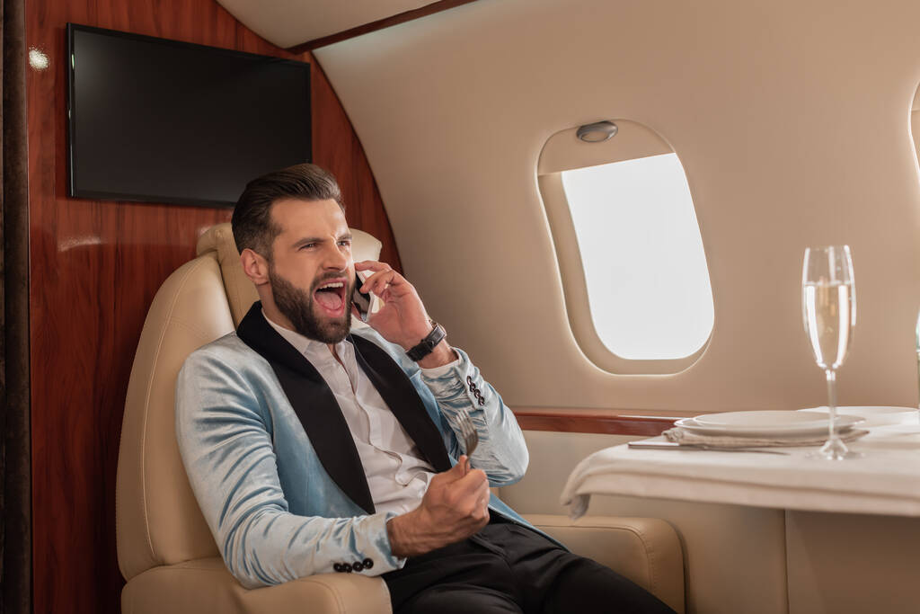θυμωμένος άνθρωπος ουρλιάζοντας, ενώ μιλάμε στο smartphone σε ιδιωτικό αεροπλάνο - Φωτογραφία, εικόνα