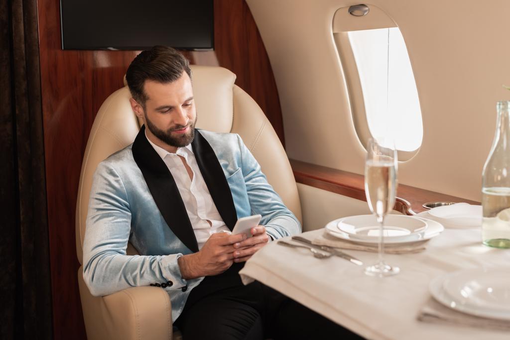 elegante man chatten op smartphone tijdens het zitten aan tafel geserveerd in prive jet - Foto, afbeelding