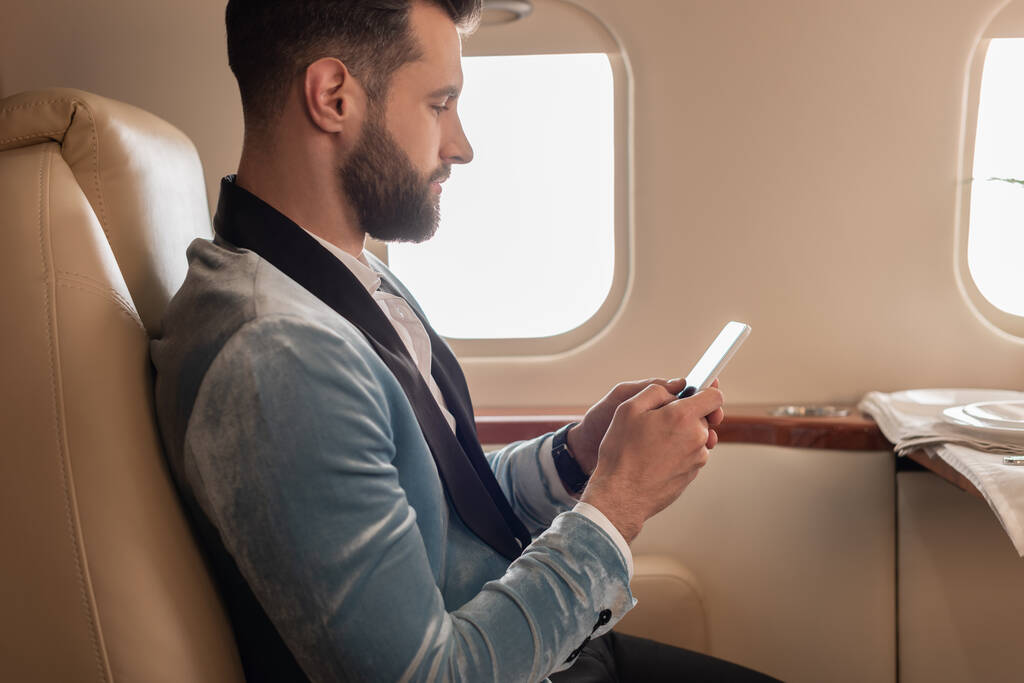 side view of elegant young man chatting on smartphone in private plane - Photo, Image