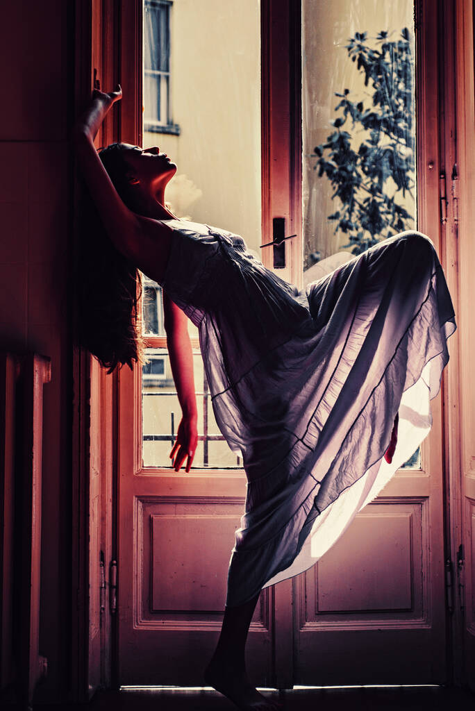 Nainen tapaa aamulla lähellä parveketta. Rentoudu Nuori nainen seisoo ikkunan lähellä. Eroottinen yöpaita. Intohimo ja kiusaus. Hän on onnellinen.. - Valokuva, kuva