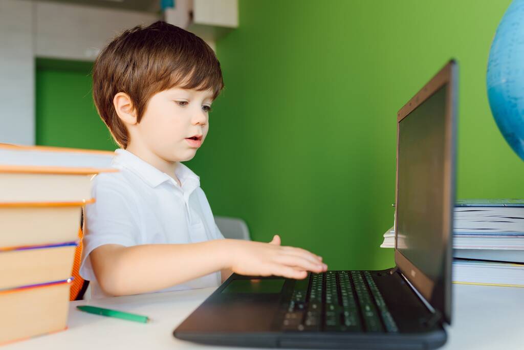Chłopiec uczy się w domu podczas kwarantanny CoVid-19, uczy się na odległość online z laptopem, dziecko odrabia lekcje do szkoły. Uczeń został w domu.. - Zdjęcie, obraz