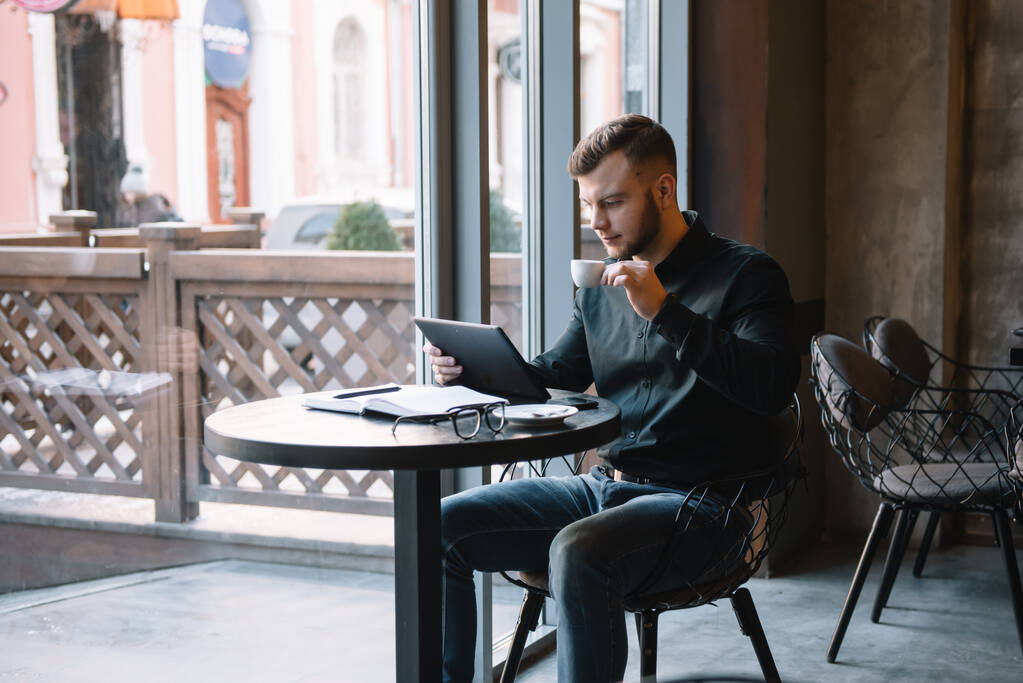 Beau homme d'affaires utilisant une tablette numérique et boire du café tout en étant assis dans un café dans le centre-ville
 - Photo, image