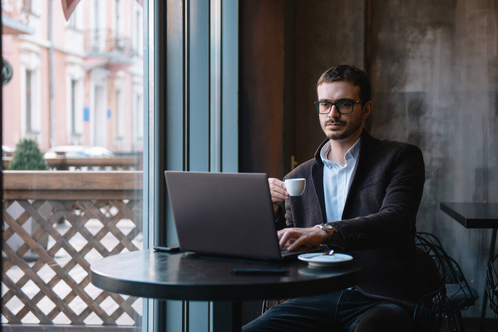 Молодой успешный бизнесмен, работающий на ноутбуке, сидя в кафе. - Фото, изображение