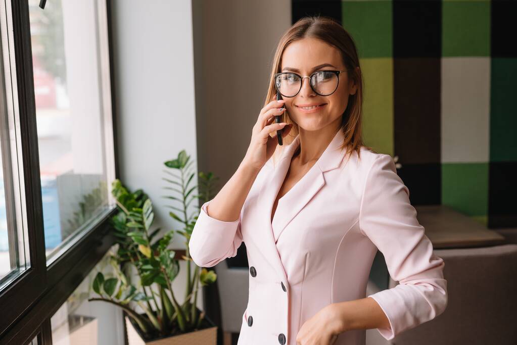 Business woman on the phone at office. Young business woman having phone call at the office. Smiling business woman. Pretty young business using smartphone at the office. - Photo, Image