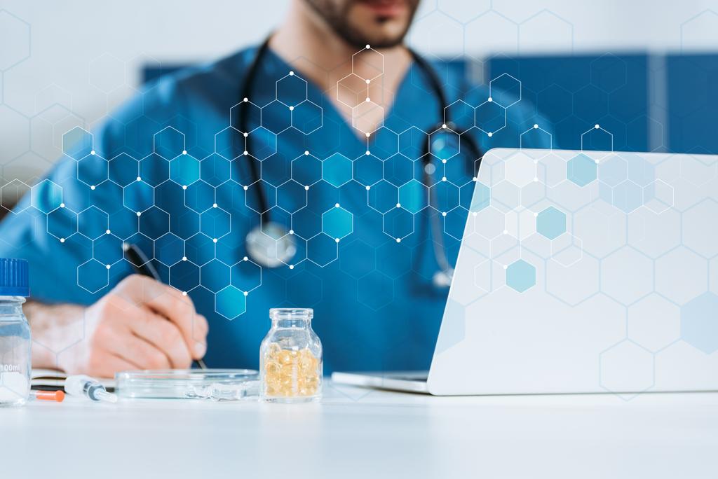 селективное внимание молодого врача, пишущего рядом с ноутбуком и контейнером с лекарствами
 - Фото, изображение