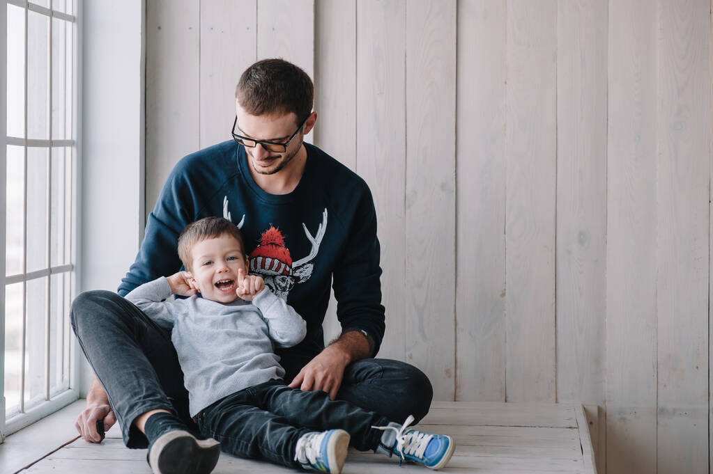 šťastný muž a jeho paže objímají svého syna. Rodinný modus doma na gauči. Bílá košile. Den otců - Fotografie, Obrázek