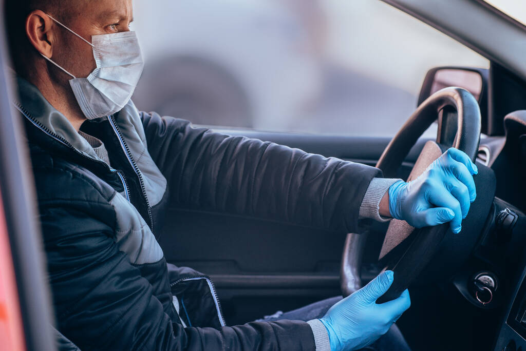 Ein Mann am Steuer eines Autos mit Schutzmaske und Handschuhen. Sichere Fahrt im Taxi während einer Coronavirus-Pandemie. Fahrer und Passagiere in Quarantäne vor Bakterien und Viren schützen. - Foto, Bild