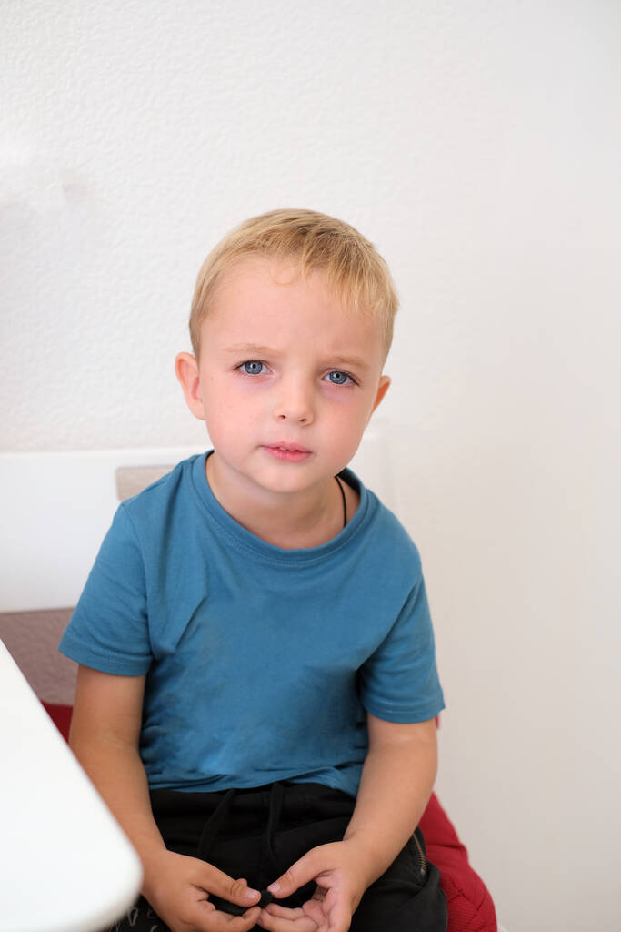 Portrét malého chlapce, bělocha, sedícího v křesle. malý čtyřletý chlapec s blond vlasy a modrýma očima sedí na židli - Fotografie, Obrázek