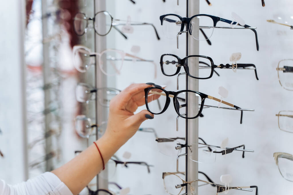 Gözlük seçiyorum. Optikteki müşteri. Elimizdeki seçici odaklanma. Gözlüklü, düzeltici gözlüğe dokunan bir kadın. Dükkanda geniş çeşitlilik. - Fotoğraf, Görsel