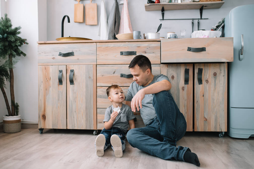若い男と台所でオーブンシートを持つ彼の息子。台所に息子のいる父 - 写真・画像