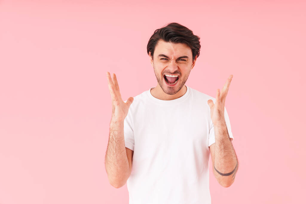 Afbeelding van Kaukasische woedende man met borstelharen schreeuwen op de camera met gooien omhoog handen geïsoleerd over roze achtergrond - Foto, afbeelding