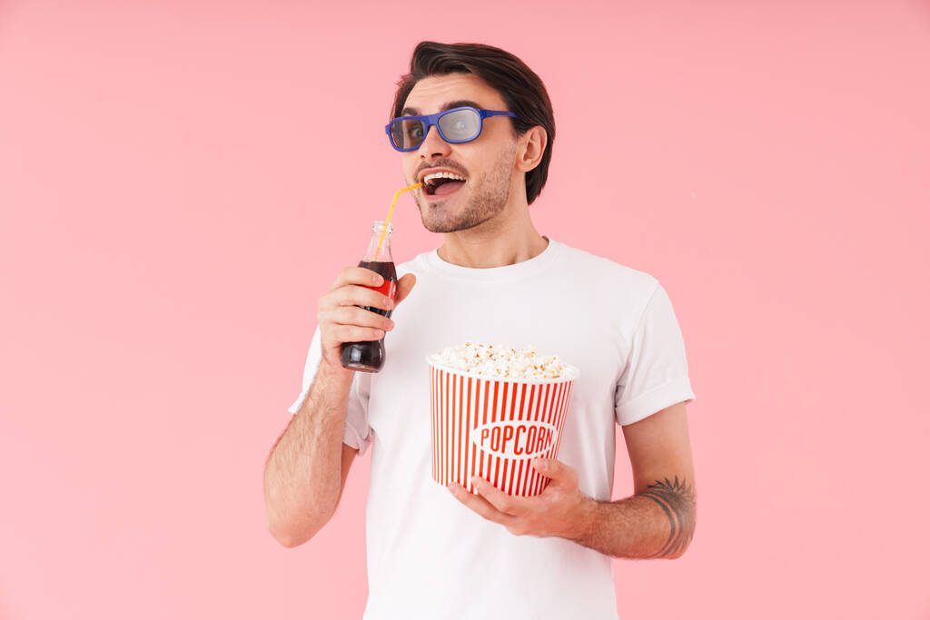 Imagen del hombre excitado en gafas 3D sosteniendo cubo con palomitas de maíz y botella de refresco aislado sobre fondo rosa
 - Foto, imagen