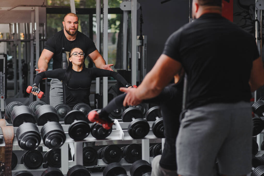 Fitness, sport, gyakorlatok és súlyemelés. Koncepció - egy fiatal nő és egy fiatal férfi súlyzókkal söpri az izmokat az edzőteremben. - Fotó, kép