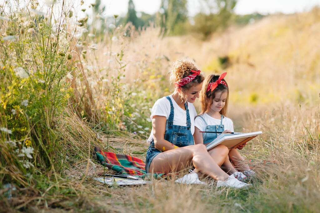 Genç çekici anne, kızına yaz parkında resim yapmayı öğretiyor. Okul çağındaki çocuklar için açık hava aktivitesi - Fotoğraf, Görsel