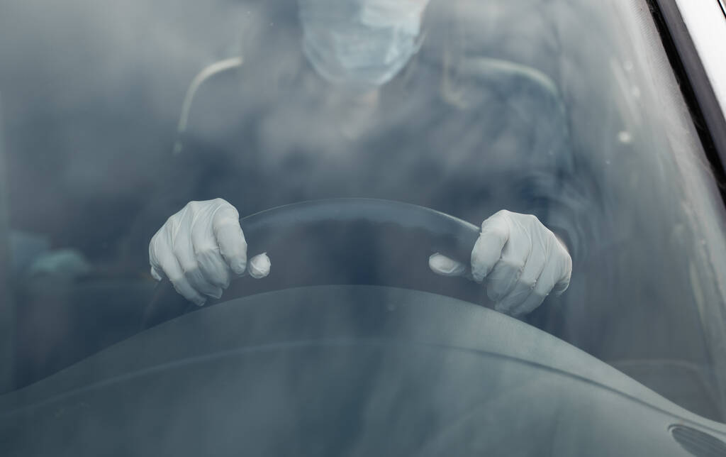 Vrouw in beschermend pak, medisch masker en rubberen handschoenen ter bescherming tegen bacteriën en virussen rijdt in een auto. Beschermend masker tijdens quarantaine, wereldpandemie, covid 19, coronavirus, infectie. - Foto, afbeelding