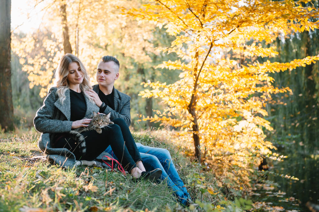 Schönes junges Paar, das sich im Herbstpark ausruht. Herbstkonzept. Liebespaar rastet mit seiner Katze aus. - Foto, Bild