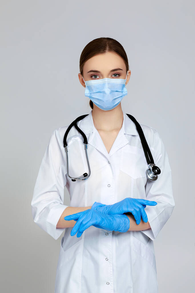 Portret van een mooie vrouwelijke arts in witte labjas en stethoscoop geïsoleerd op grijze achtergrond - Foto, afbeelding