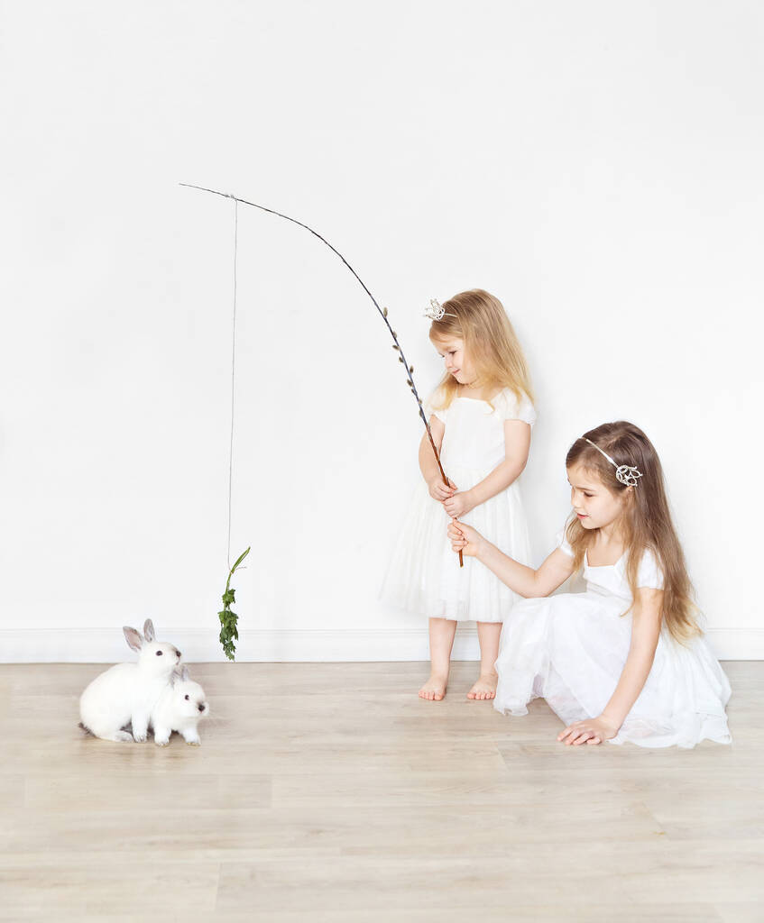 Девочки в белых платьях кормят кроликов травой
. - Фото, изображение