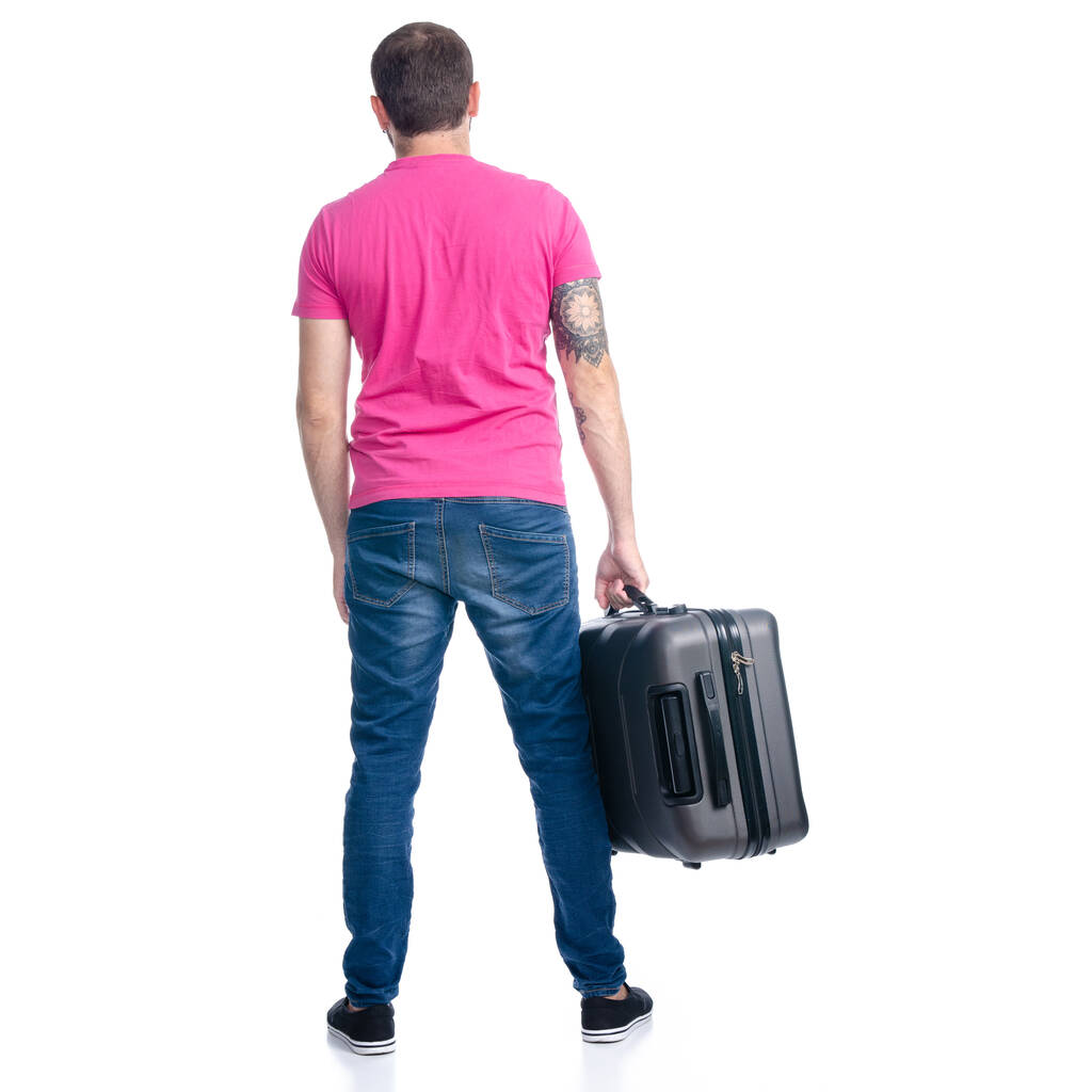 Mężczyzna w dżinsach trzyma walizkę na stojąco. - Zdjęcie, obraz