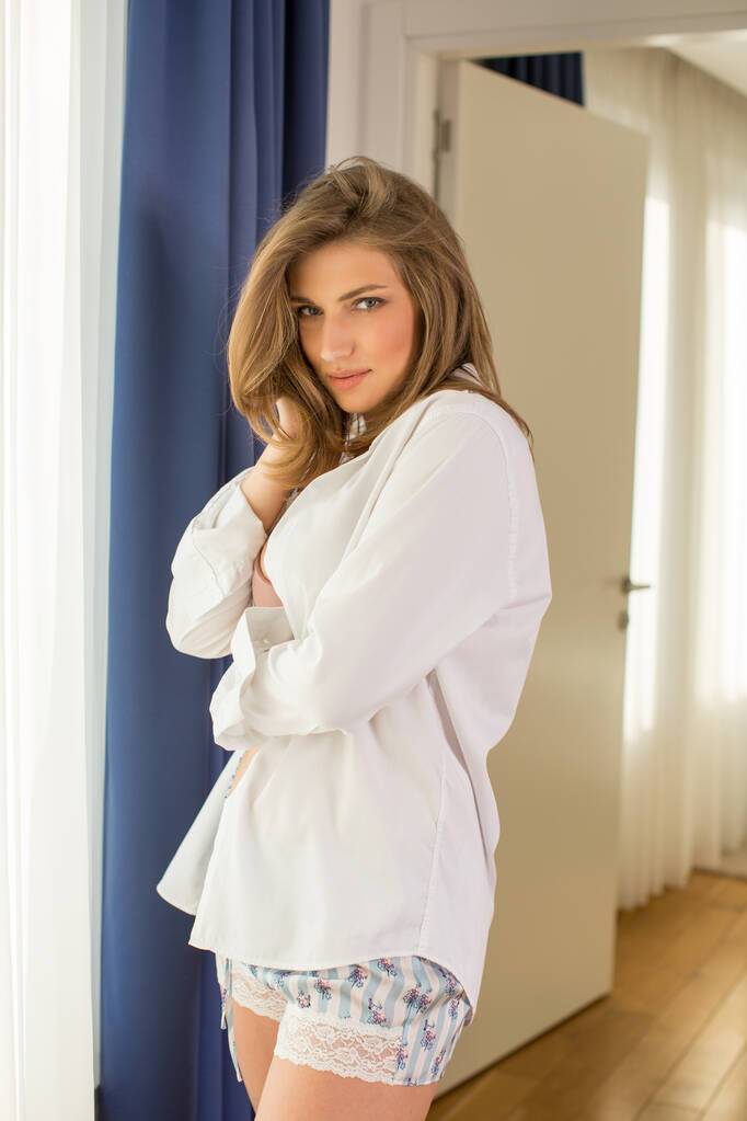 Aantrekkelijke jonge vrouw in hemd en ondergoed poserend in hotelkamer - Foto, afbeelding