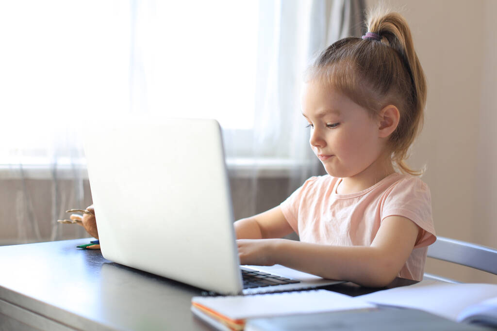 Uczenie się na odległość. Wesoła dziewczynka korzystająca z laptopa studiującego przez internetowy system e-learningowy - Zdjęcie, obraz