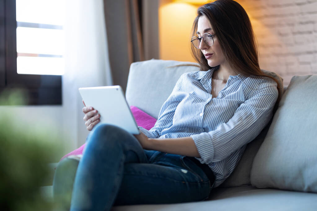 Girato di bella giovane donna utilizzando il suo tablet digitale per la lettura mentre seduto sul divano a casa
. - Foto, immagini
