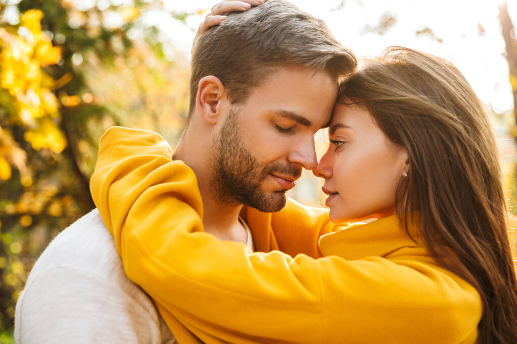 Imagen de atractiva pareja caucásica joven enamorada abrazándose mientras camina en el parque de otoño
 - Foto, Imagen