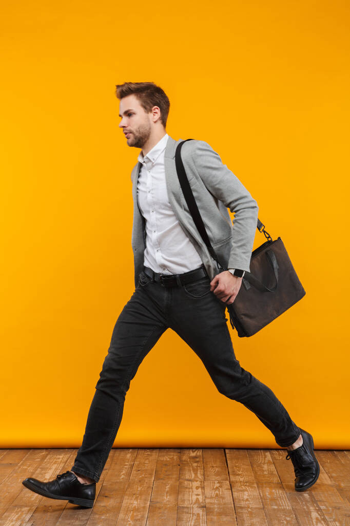 Comprimento total de um belo jovem empresário vestindo jaqueta andando sobre fundo amarelo
 - Foto, Imagem