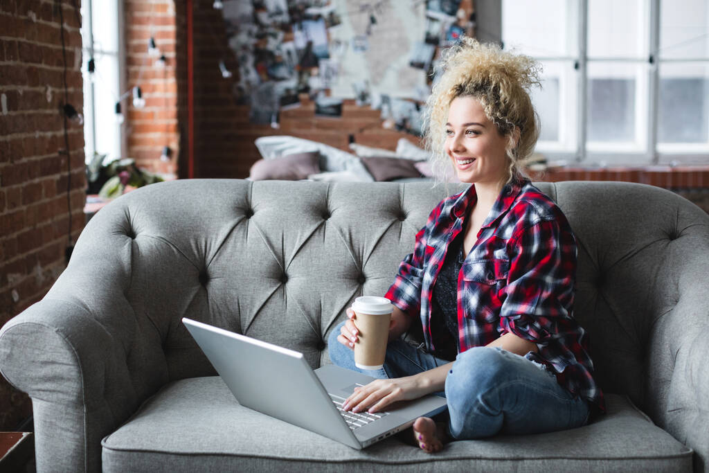 Smiling beautiful woman on sofa with laptop and coffee. Freelancer. - Photo, Image