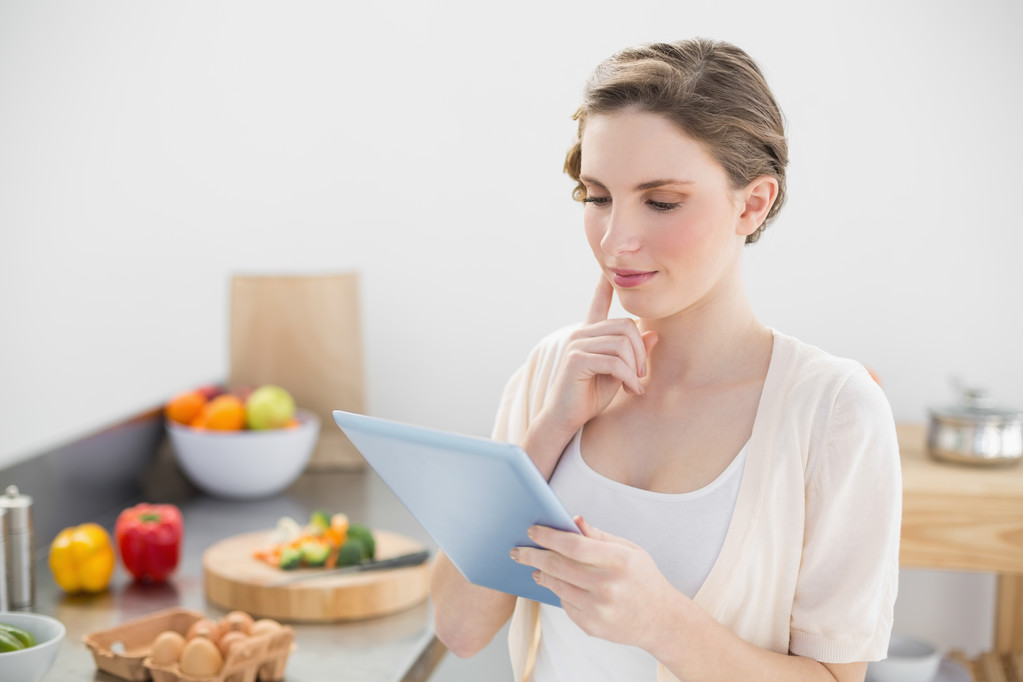Concentration jeune femme en utilisant sa tablette debout dans sa cuisine
 - Photo, image
