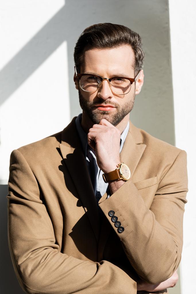 pensive businessman in glasses touching face and looking at camera - Photo, Image
