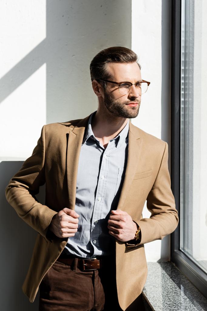 bearded businessman looking at window and touching blazer  - Photo, Image