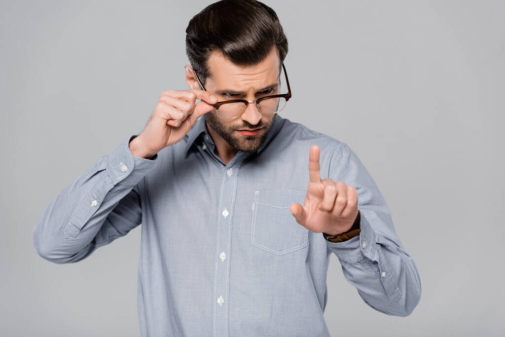 bel homme d'affaires touchant des lunettes et pointant du doigt isolé sur gris
  - Photo, image
