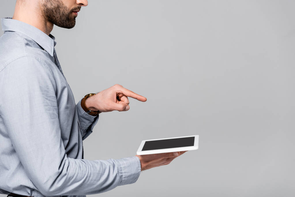 Ausgeschnittene Ansicht eines Geschäftsmannes, der mit dem Finger zeigt und ein digitales Tablet mit leerem Bildschirm hält, isoliert auf grau  - Foto, Bild