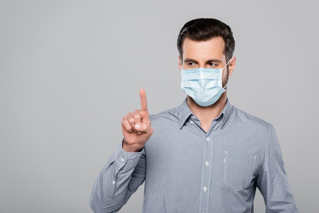 hombre de negocios en máscara médica señalando con el dedo aislado en gris
 - Foto, Imagen